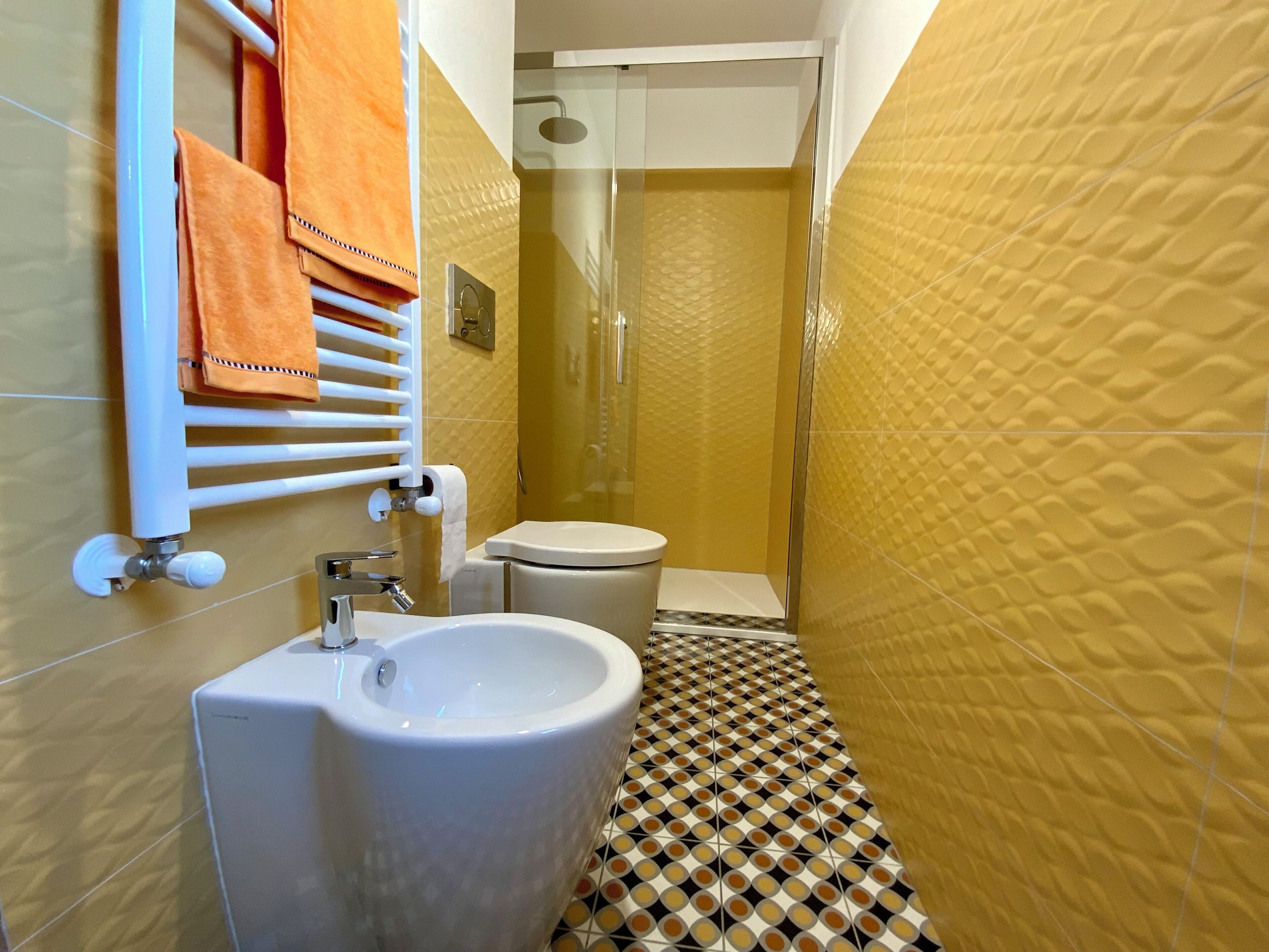 A bathroom with a white sink, toilet, and shower. The walls are tiled with a yellow pattern, and the floor has a black and white checkered design.