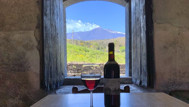 Une bouteille de vin et un verre sur une table, avec vue sur une montagne à travers une fenêtre en arc de cercle.