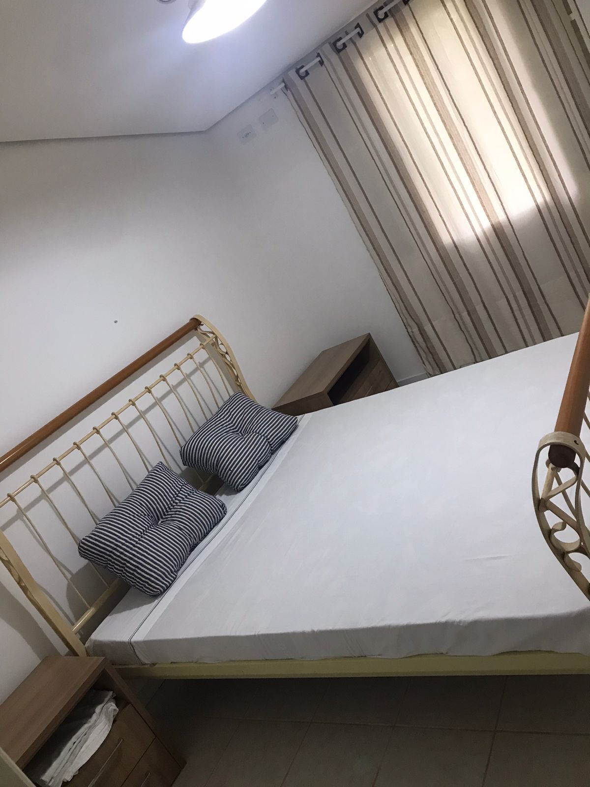 Una habitación pequeña con cama individual, cabecera y mesita de noche de madera, además de una cortina.