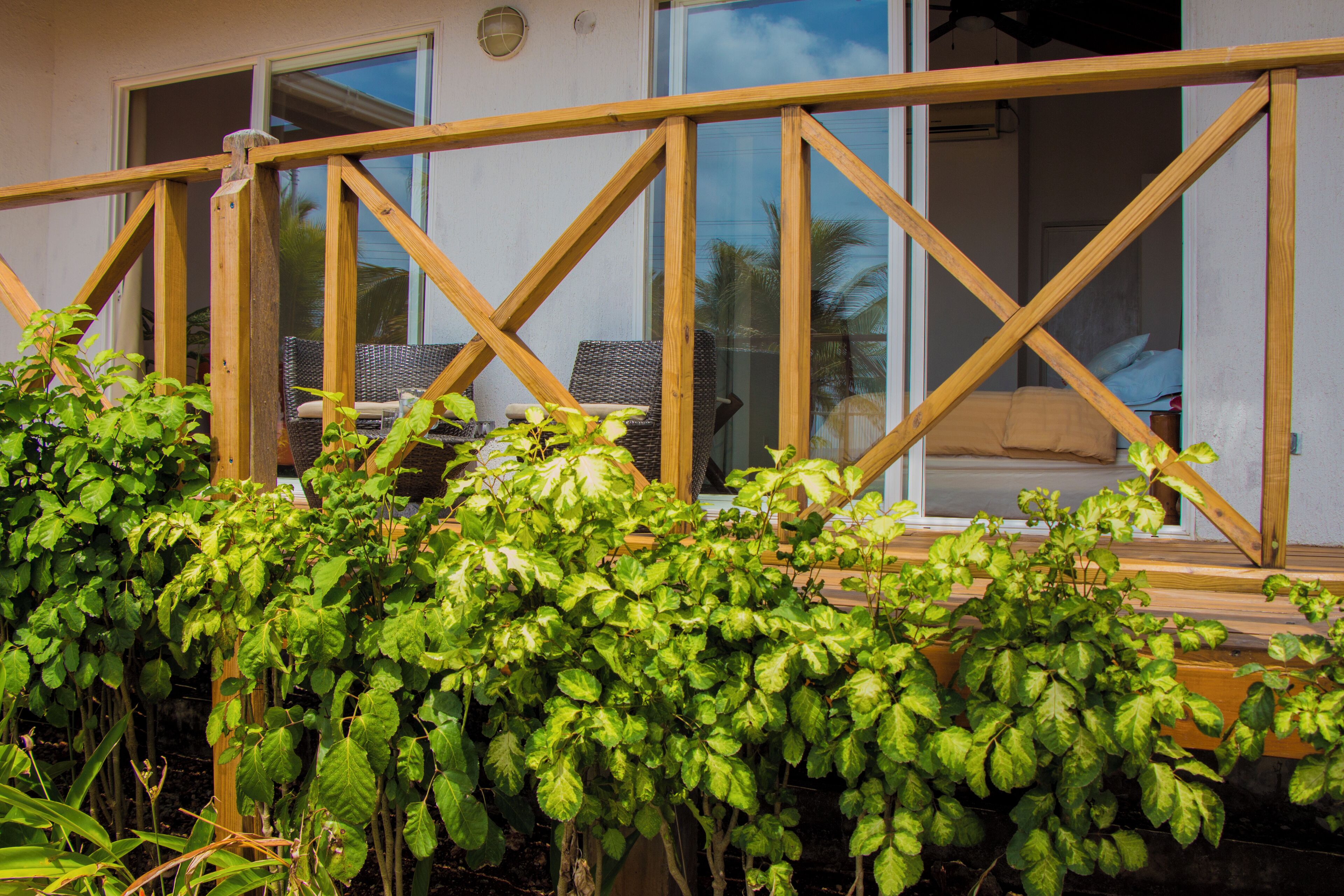 Une terrasse en bois dotée d’une balustrade en verre, de meubles en osier et d’une végétation luxuriante.