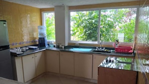A kitchen with a tiled backsplash, a window with a view of greenery, and a sink with a red dish rack. - Playa Tranquilo B&B  (San Andrés)