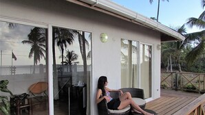 A room with a large sliding glass door, a wicker sofa, and a wooden deck. - Playa Tranquilo B&B  (San Andrés)