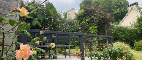 Eine Holzterrasse mit schwarzer Geländer, umgeben von üppigem Grün und blühenden Pflanzen.