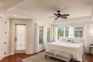 Quarto com uma cama grande, um ventilador de teto e vista para o exterior pelas janelas.