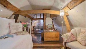 Une chambre confortable située sous les toits, avec des poutres apparentes, un lit en bois, une petite table et une chaise.