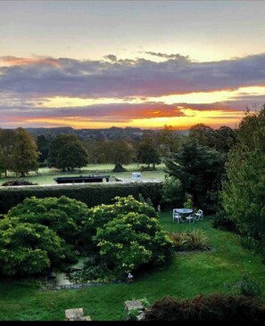 Een vredig landschap met een zonsondergang, weelderige begroeiing en een verre blik op een golfbaan.
