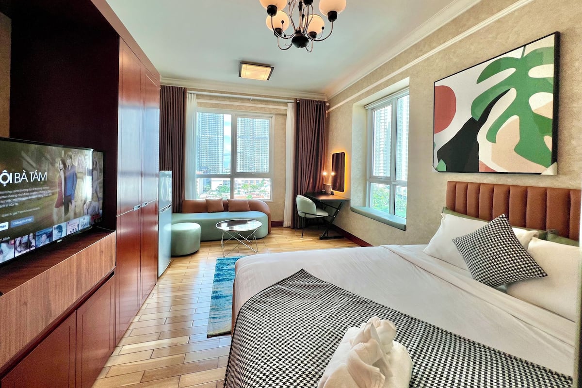 A modern hotel room with a large bed, a desk, a sofa, and a television.