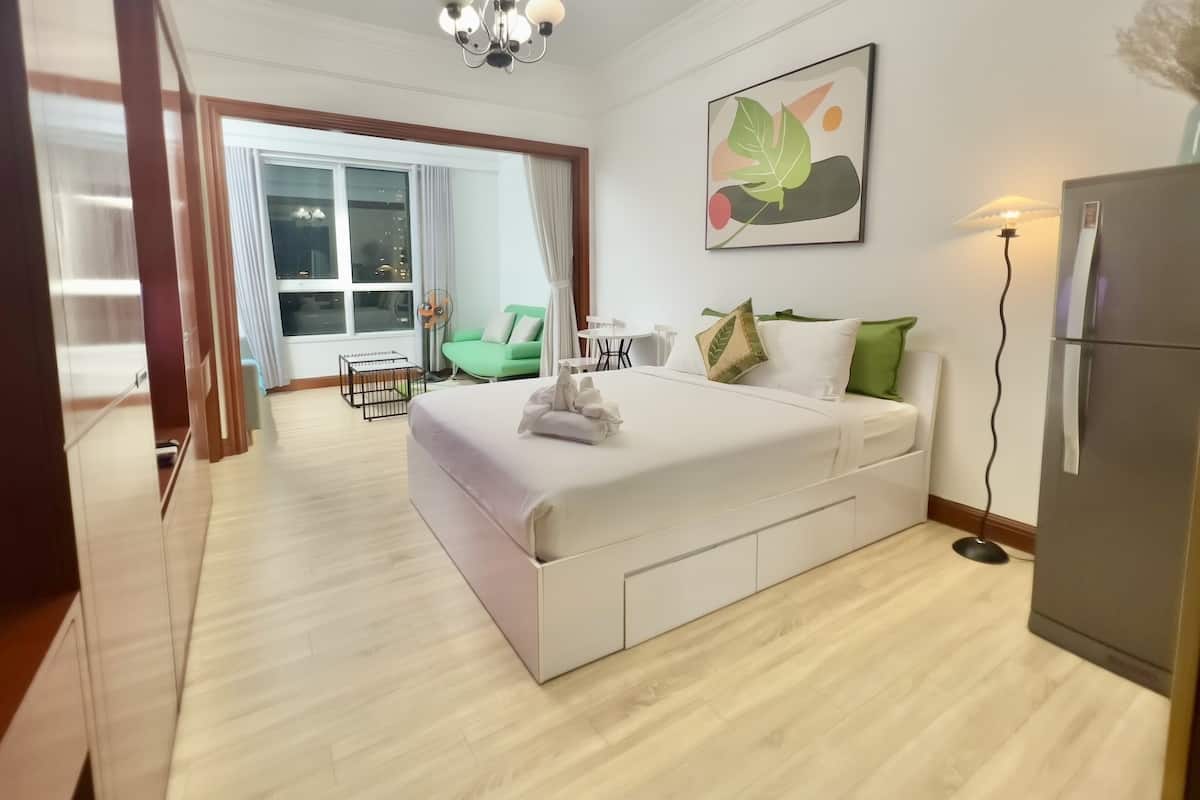 A modern hotel room with a large bed, a dining area, and a view of the city at night.