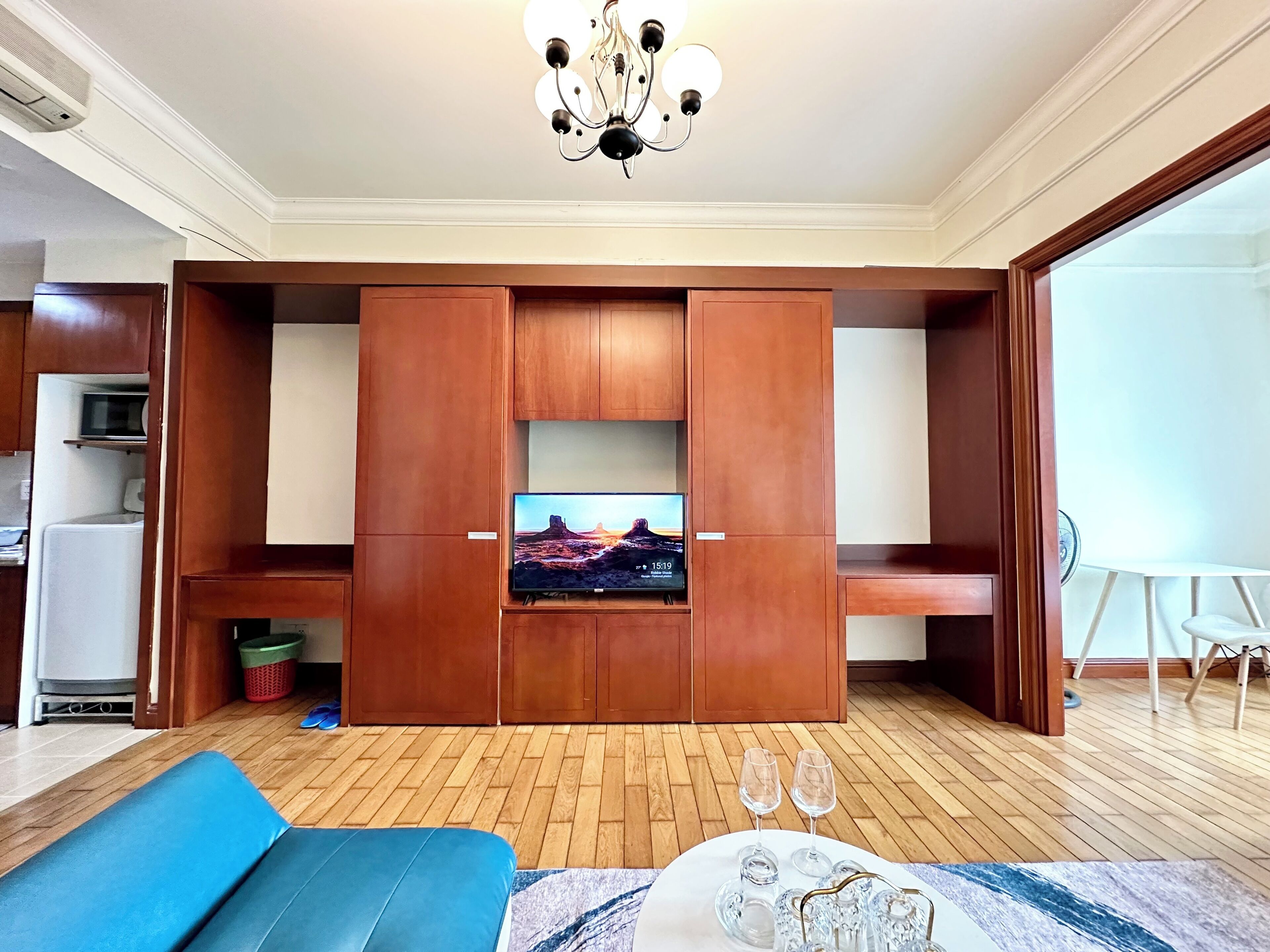Ein Wohnzimmer mit Flachbildfernseher, Holzschränken, einem blauen Sofa und einem Esstisch mit Gläsern.