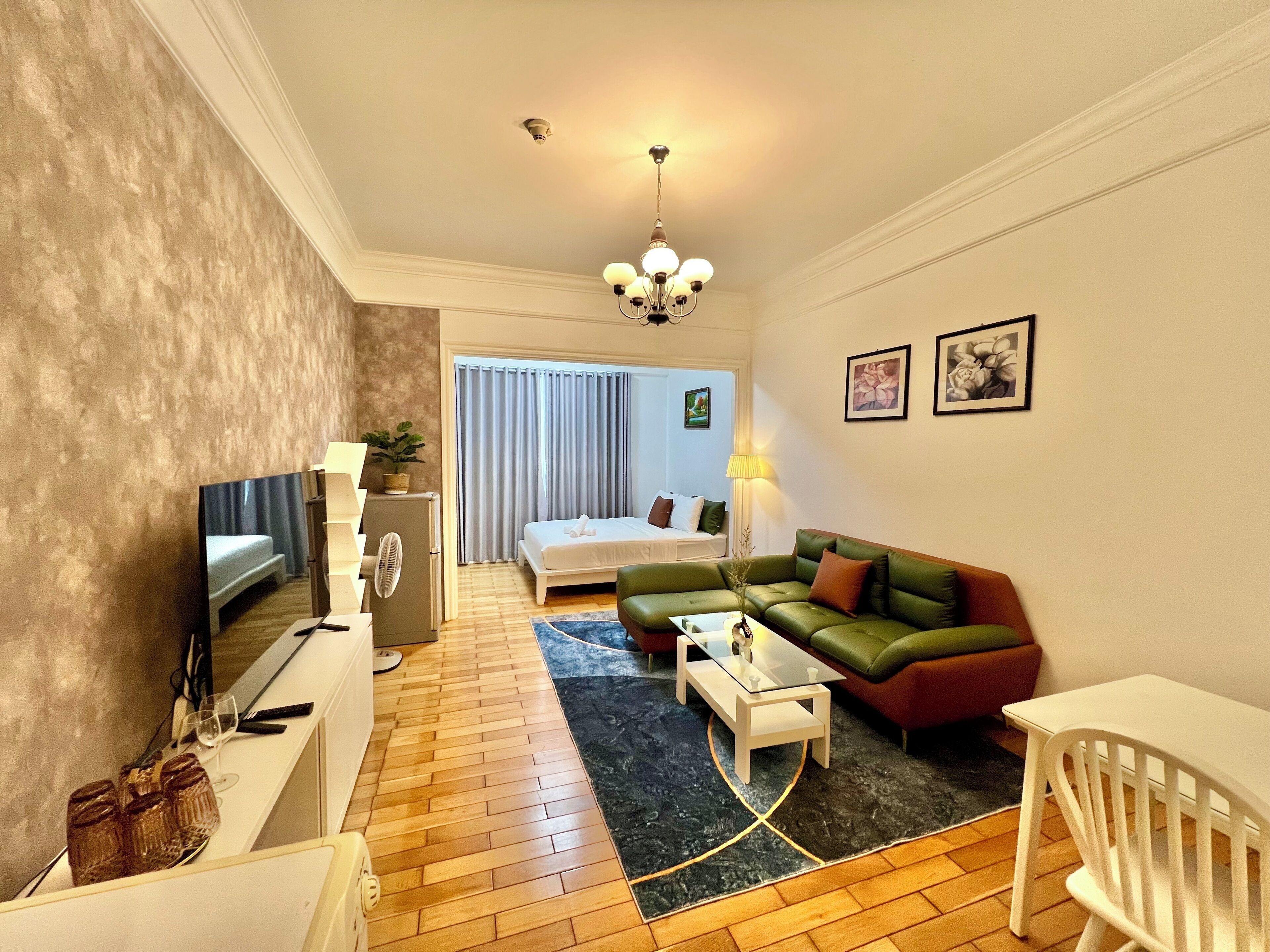 A compact hotel room with a bed, a green sofa, a white table, and a TV.