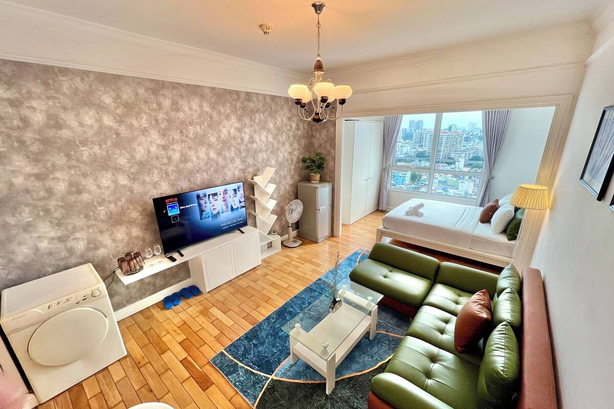 A modern living room with a flat-screen TV, a sofa, a coffee table, and a view of the city through large windows.