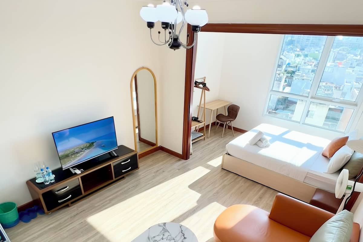 A modern living room with a sofa, a TV, a wooden desk, and a large window with a city view.