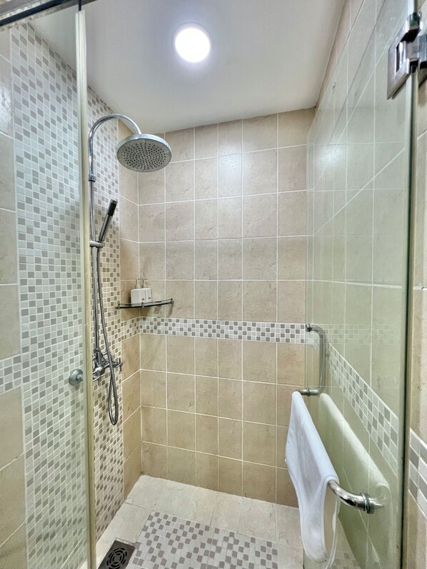 A shower with a glass door, a handheld showerhead, and a towel rack.