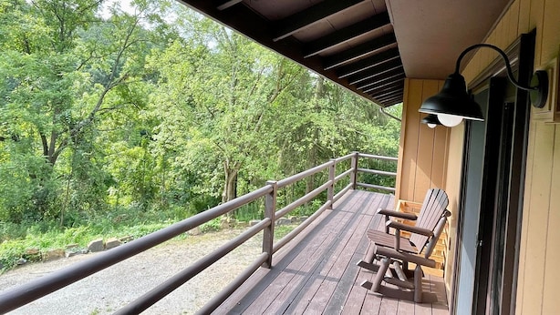 Eine Holzterrasse mit Geländer, einer Bank und einem Tisch, mit Blick auf eine bewaldete Landschaft.