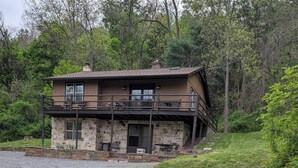 Ein zweistöckiges Steinhaus mit Balkon, umgeben von einer Rasenfläche und Bäumen.