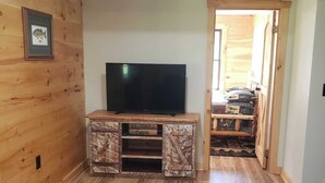 Ein Zimmer mit Holzboden, einem Fernseher auf einem Holzbodenständer und einer Tür zu einem anderen Raum.