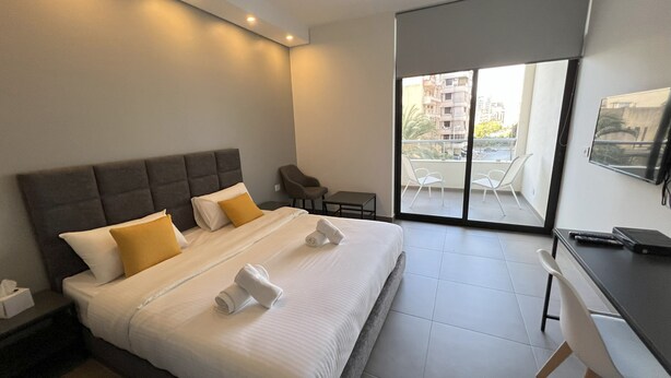 A modern hotel room with a large bed, a desk, and a balcony with a city view. - Time22 Apartment Hotel (Amaret Chalhoub)
