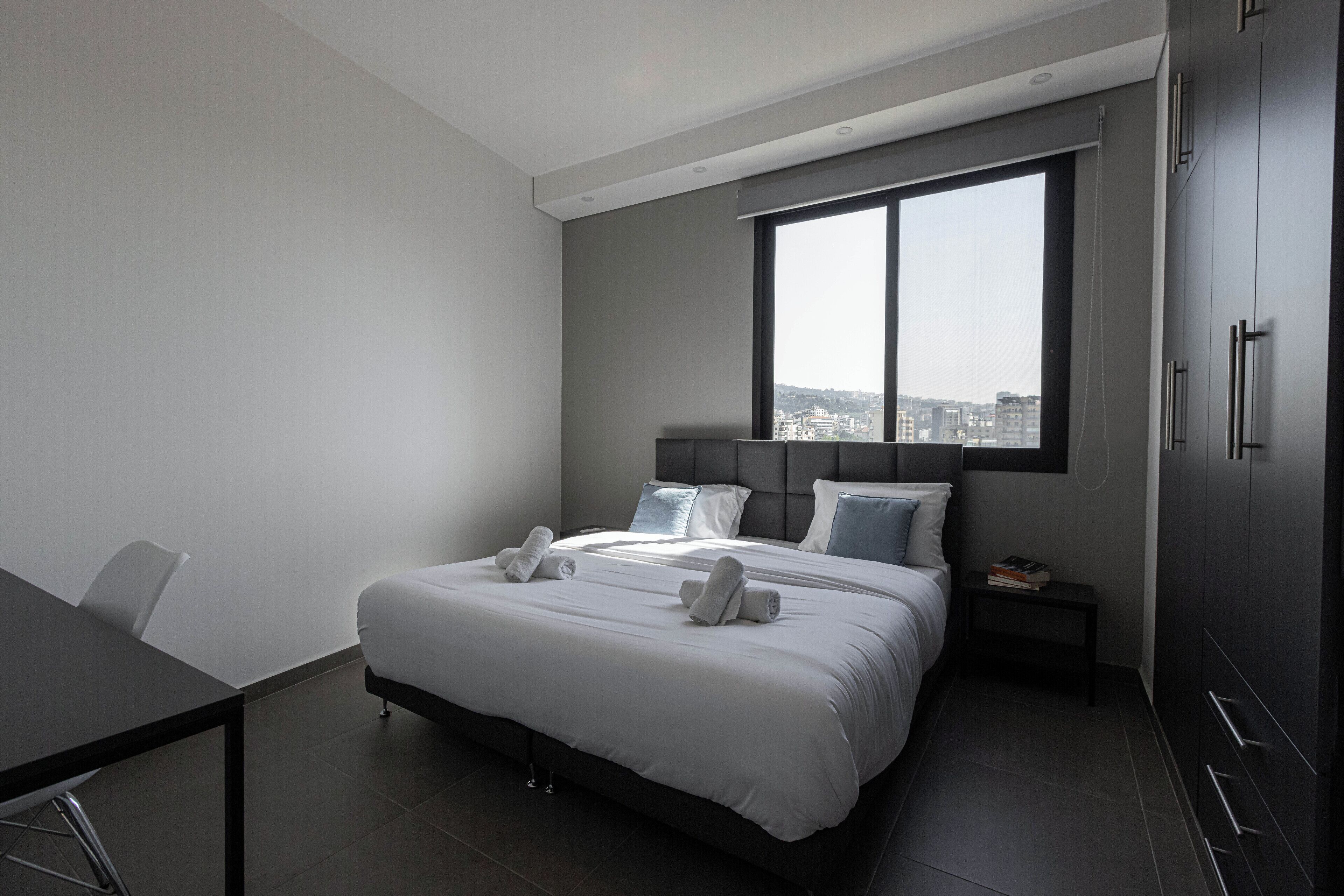 Quarto de hotel moderno com uma cama grande, uma mesa de escritório e vista da cidade através de uma ampla janela.