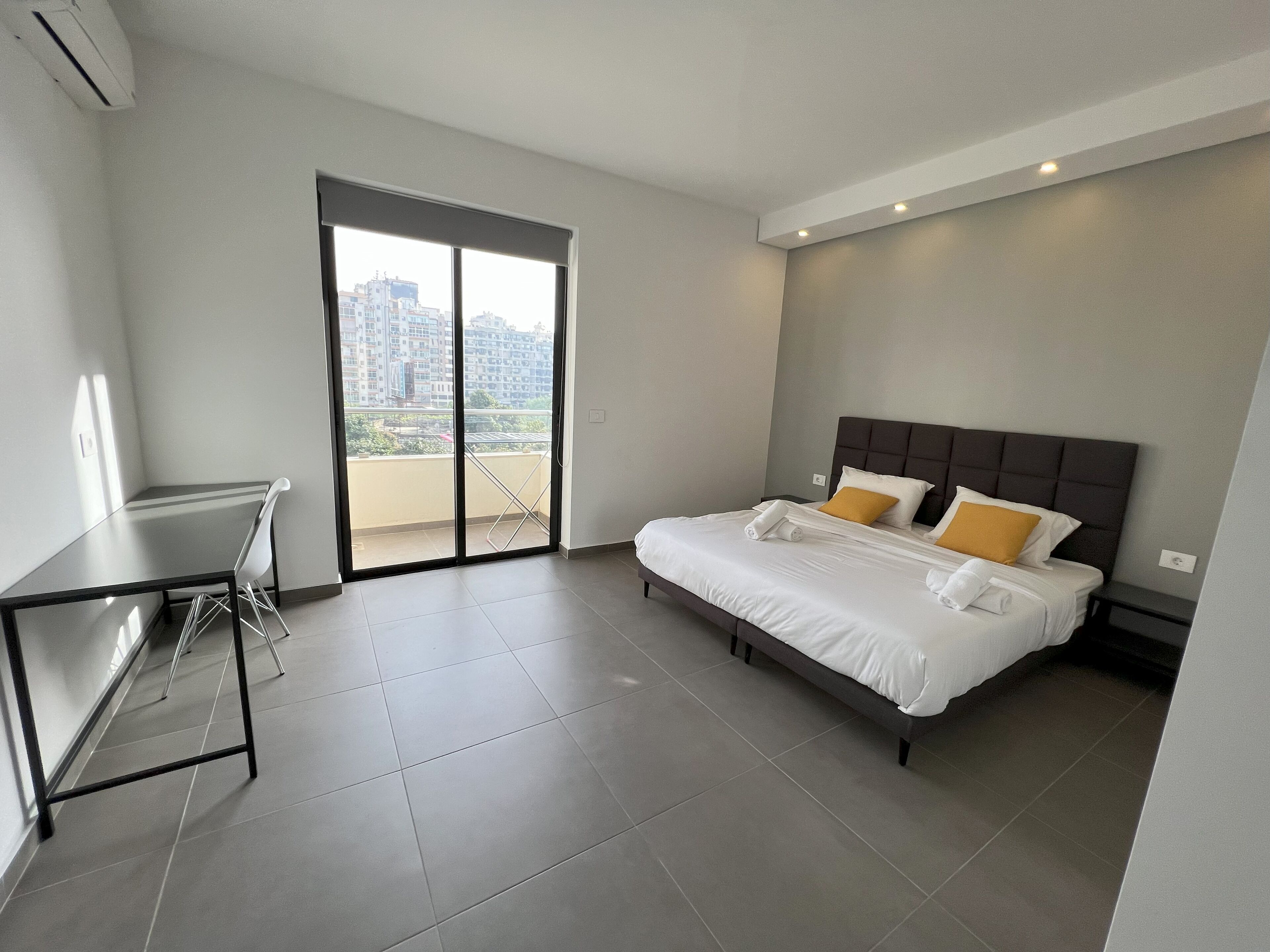 Une chambre d’hôtel moderne équipée d’un lit, d’un bureau et d’un balcon offrant une vue sur la ville.