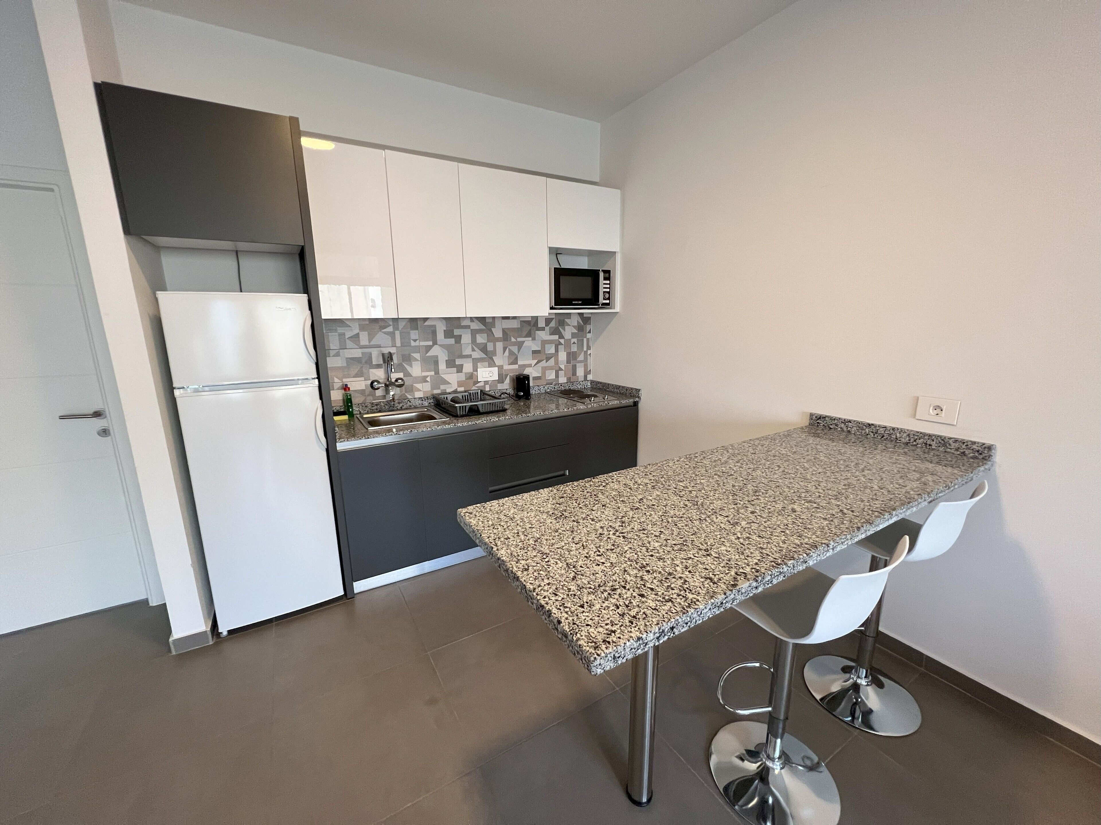 Una cocina moderna con armarios blancos, microondas integrado, encimera de granito y un taburete de bar.
