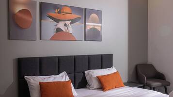A modern hotel room with a neatly made bed, a chair, and artwork on the wall.