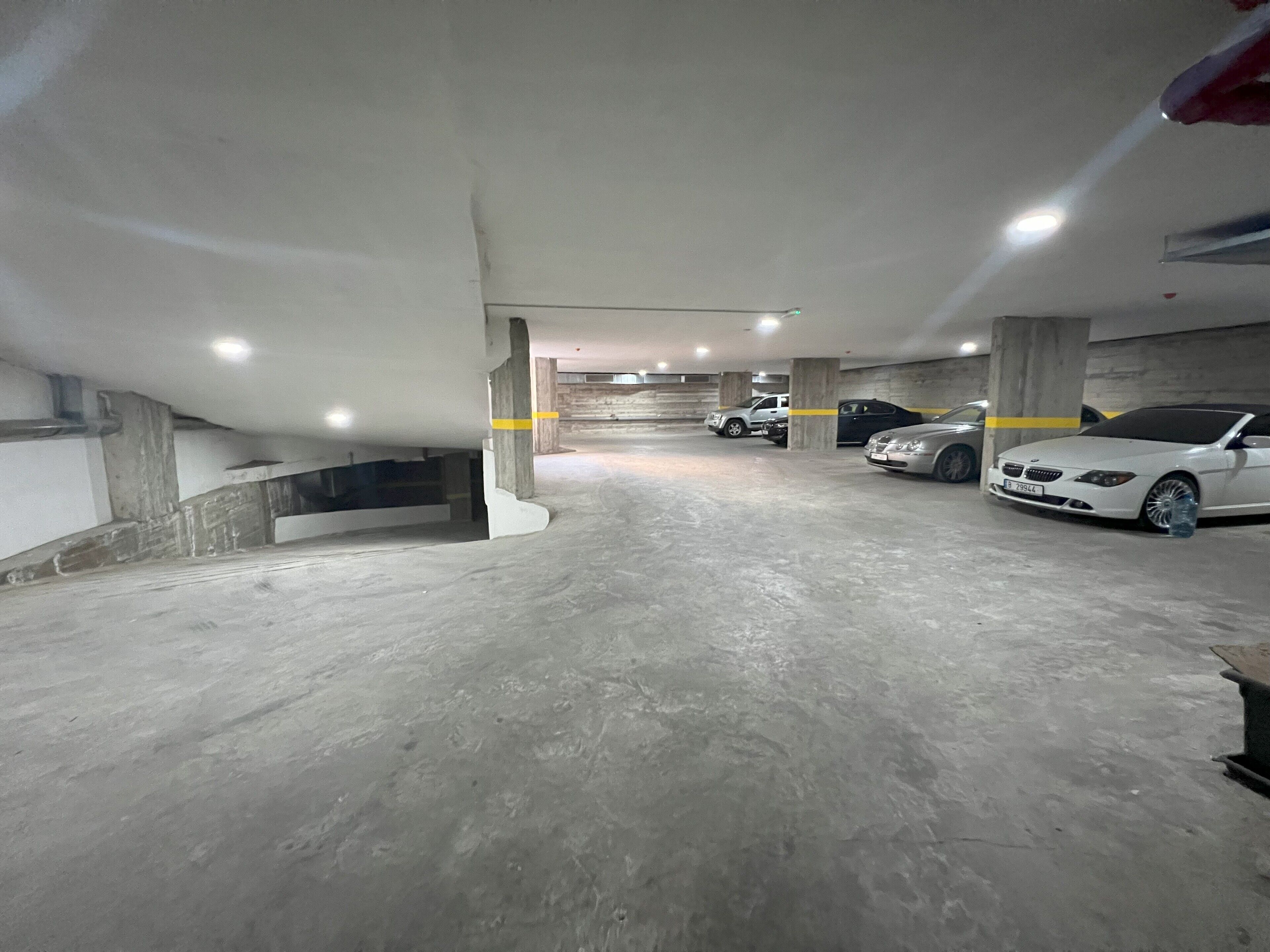 An underground parking garage with concrete pillars, a white car, and a truck parked.
