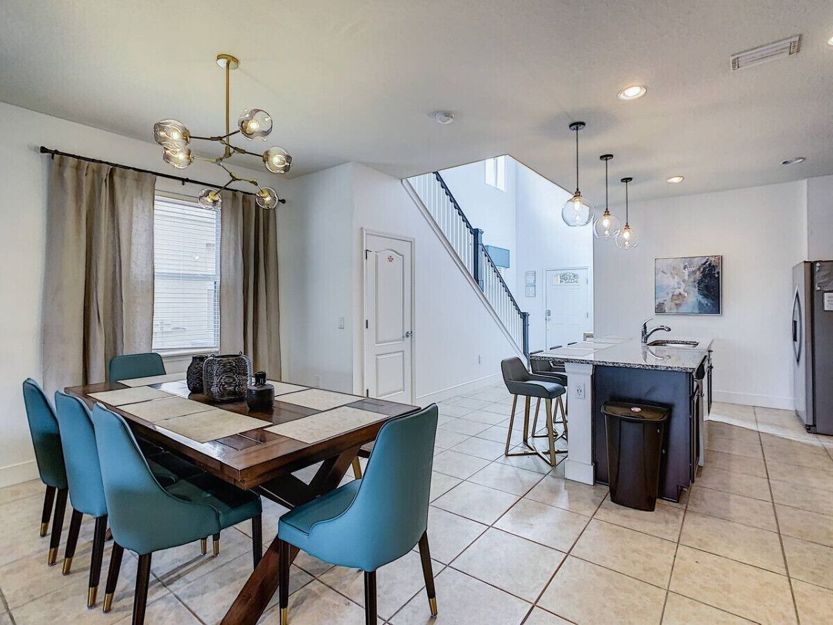 A modern kitchen with a central island, a dining area with blue chairs, and a staircase leading to an upper level.