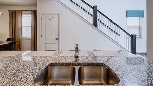 A kitchen with a granite countertop, stainless steel sink, and a staircase with a black railing. - Amazing Themed Villa with Private Pool (Kissimmee)