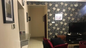 A living room with a sofa, a TV, and a patterned wallpaper. - Shortlet Apartment Milverton Estate (Lekki)
