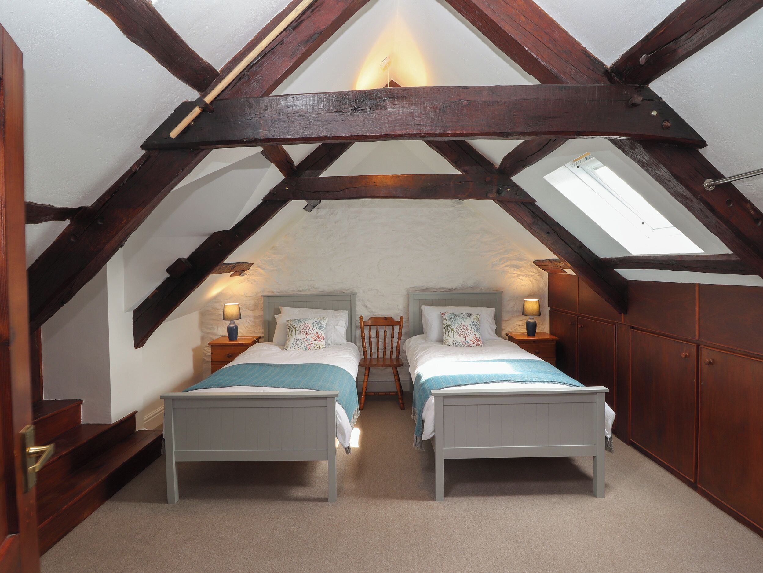 A bedroom with two beds, wooden beams, a skylight, and a stone wall.