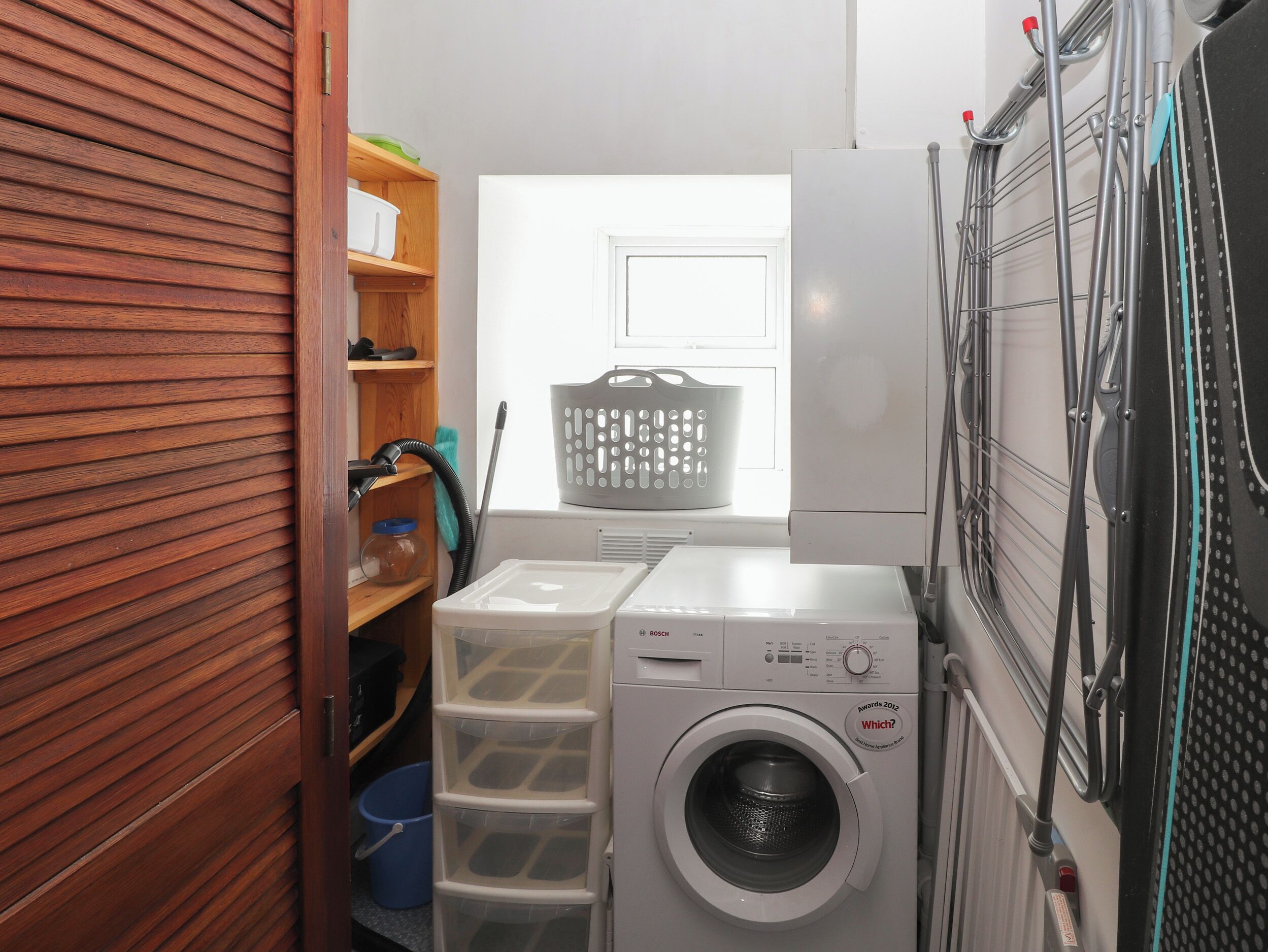 A compact laundry room with a front-loading washing machine, a drying rack, and a drying cabinet.