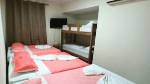 Una habitación con dos camas, cada una con ropa de cama rosa y blanca, un televisor de pantalla plana montado en la pared y un equipo de aire acondicionado sobre las camas.
