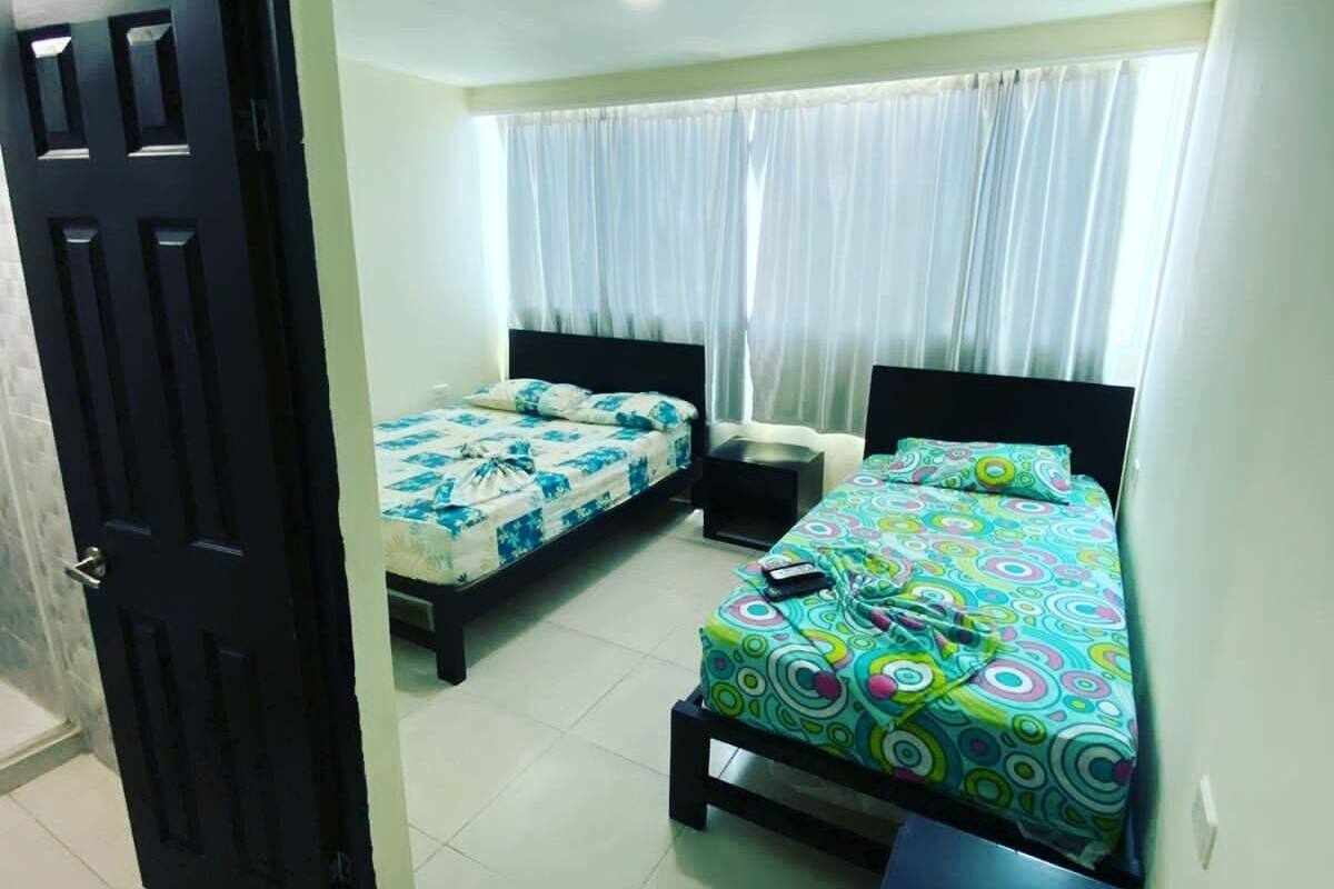 A hotel room with two single beds, a small bedside table, a nightstand, and a window with curtains.