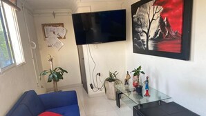 Una sala de estar con un sofá azul, una mesa de centro de vidrio, un televisor de pantalla plana y un cuadro en la pared.
