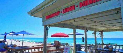 A beachside restaurant with outdoor seating and a view of the ocean.