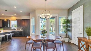 A modern kitchen with dark wood cabinets, a central island, and a dining area with a round table and chairs. - Sweet-P*Heated Private Pool (Miramar Beach)