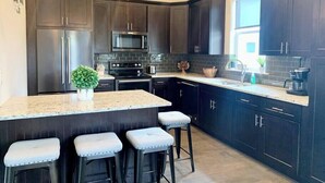 A modern kitchen with dark cabinets, stainless steel appliances, a granite countertop, and bar stools. - Sweet-P*Heated Private Pool (Miramar Beach)