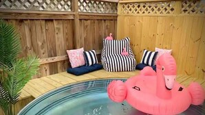 Une piscine avec un flotteur en forme de flamant rose. On y trouve des bancs en bois avec des coussins, et une clôture en treillis en arrière-plan.