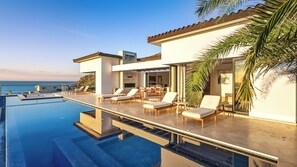 A modern poolside area with lounge chairs, a dining set, and a view of the ocean.