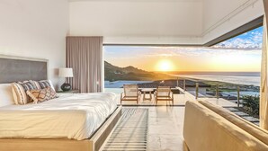 Un dormitorio con cama, mesita de noche, lámpara y vistas al atardecer sobre el océano.