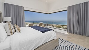 Un dormitorio con una cama grande, vistas al océano y un balcón con mobiliario exterior.