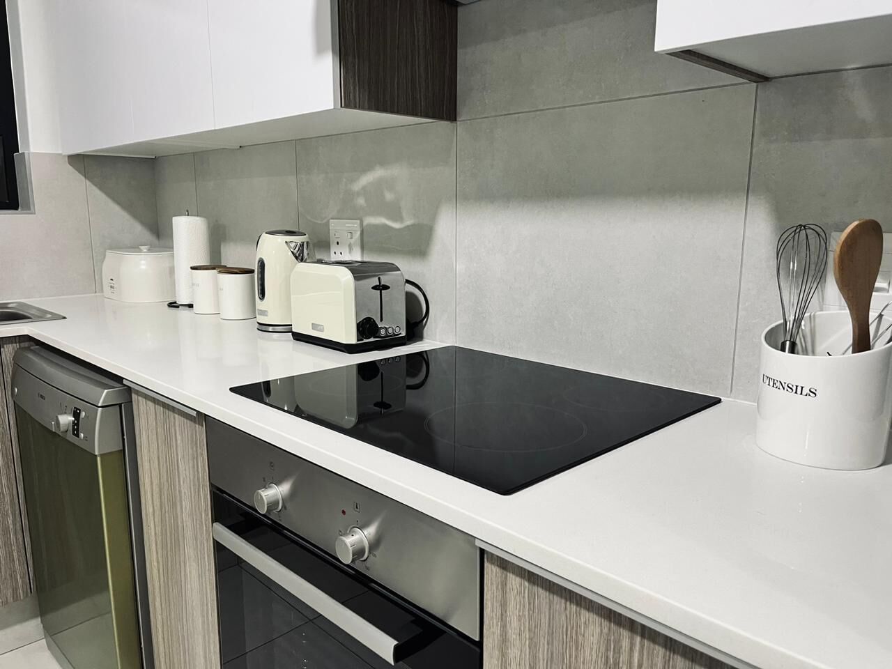 Una cocina moderna con cocina por inducción negra, horno empotrado, lavavajillas y cafetera.