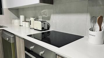 Una cocina moderna con cocina por inducción negra, horno empotrado, lavavajillas y cafetera.