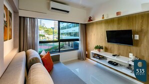 Un salon moderne avec un canapé, un téléviseur fixé au mur et une grande fenêtre avec des rideaux.