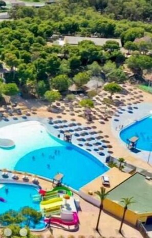 A resort with multiple swimming pools, a water slide, and lounge areas with umbrellas.