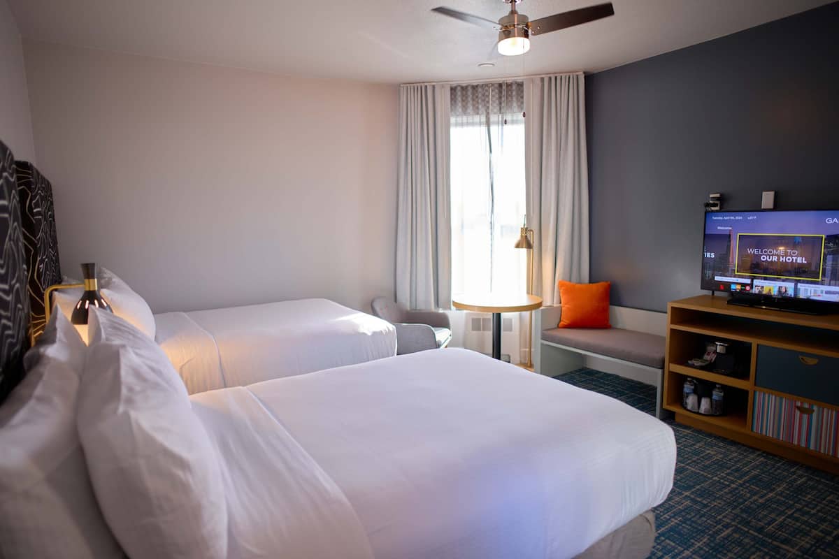 A hotel room with two beds, a television, a small table, and a window with curtains.