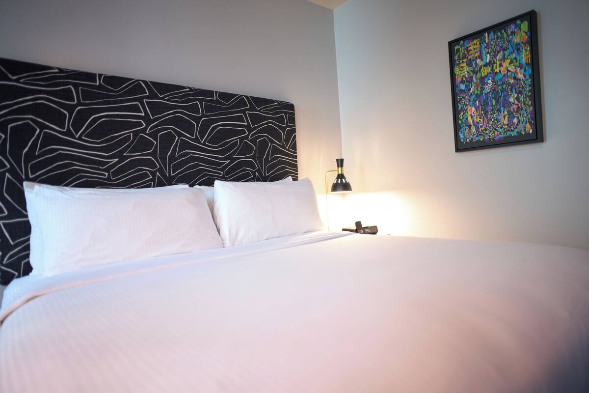 A neatly made bed with white linens and a black and white patterned headboard. A black lamp is on the nightstand beside the bed.
