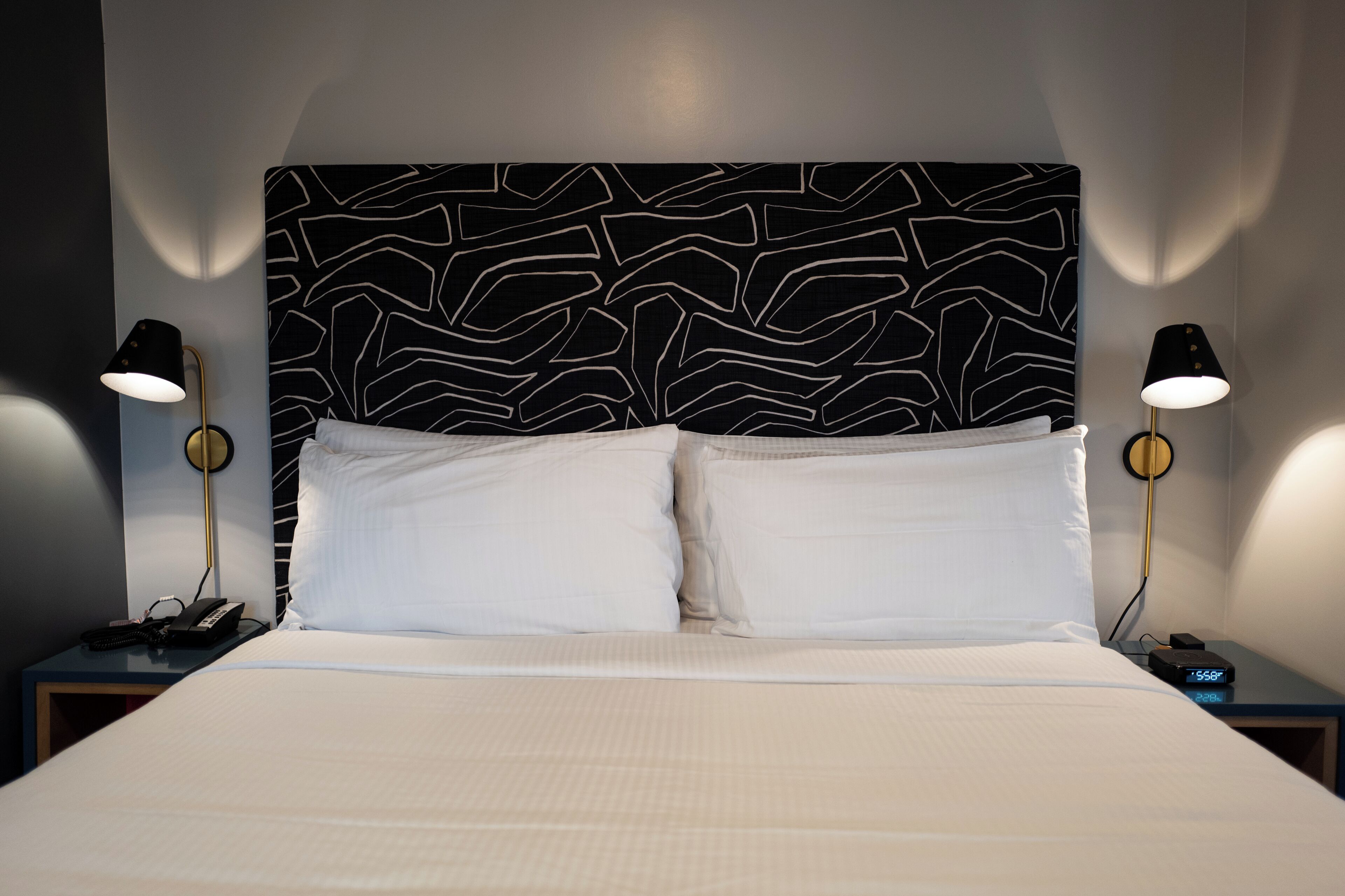 Une chambre d’hôtel avec un grand lit, deux tables de chevet et une tête de lit moderne ornée d’un motif abstrait en noir et blanc.