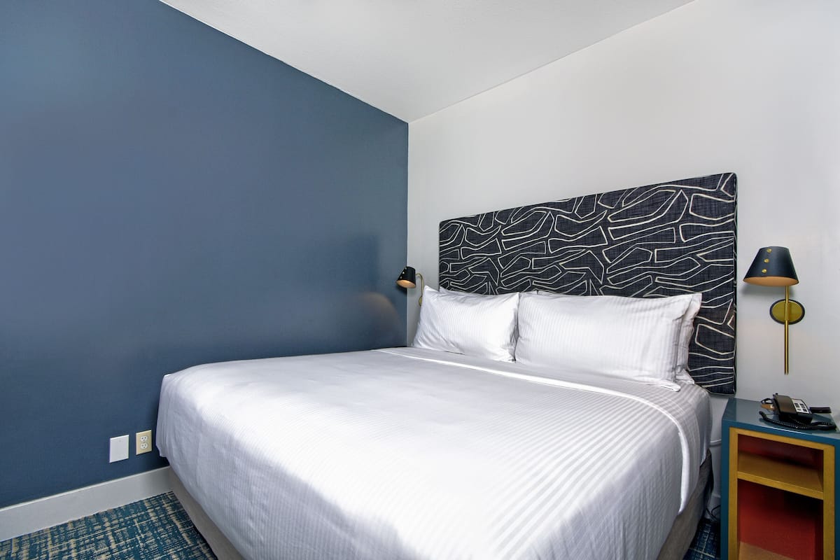 A neatly made bed with white linens in a room with blue walls and a patterned headboard.