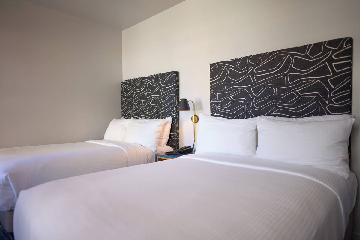 A hotel room with two beds, each with white bedding and headboards featuring a black and white abstract pattern.